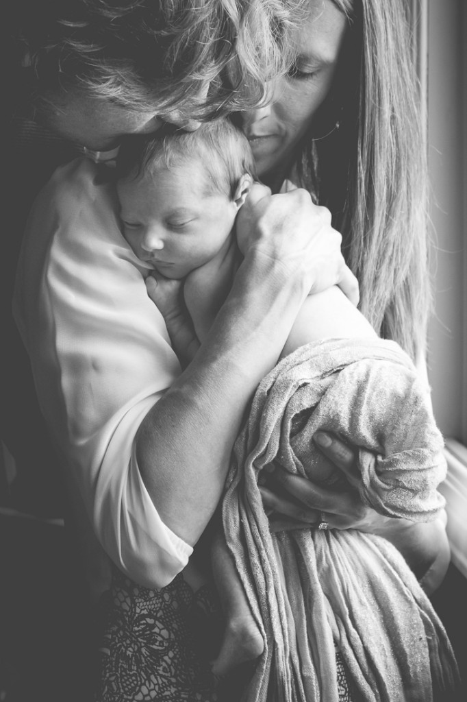 Black and white Lifestyle photo of new parents kissing their baby in their home