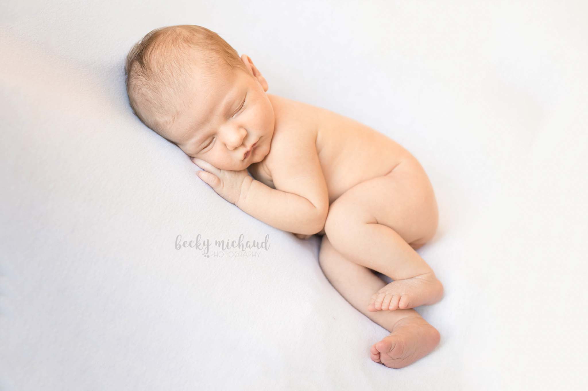 simple photo of a newborn baby lying on his side on a white blanket