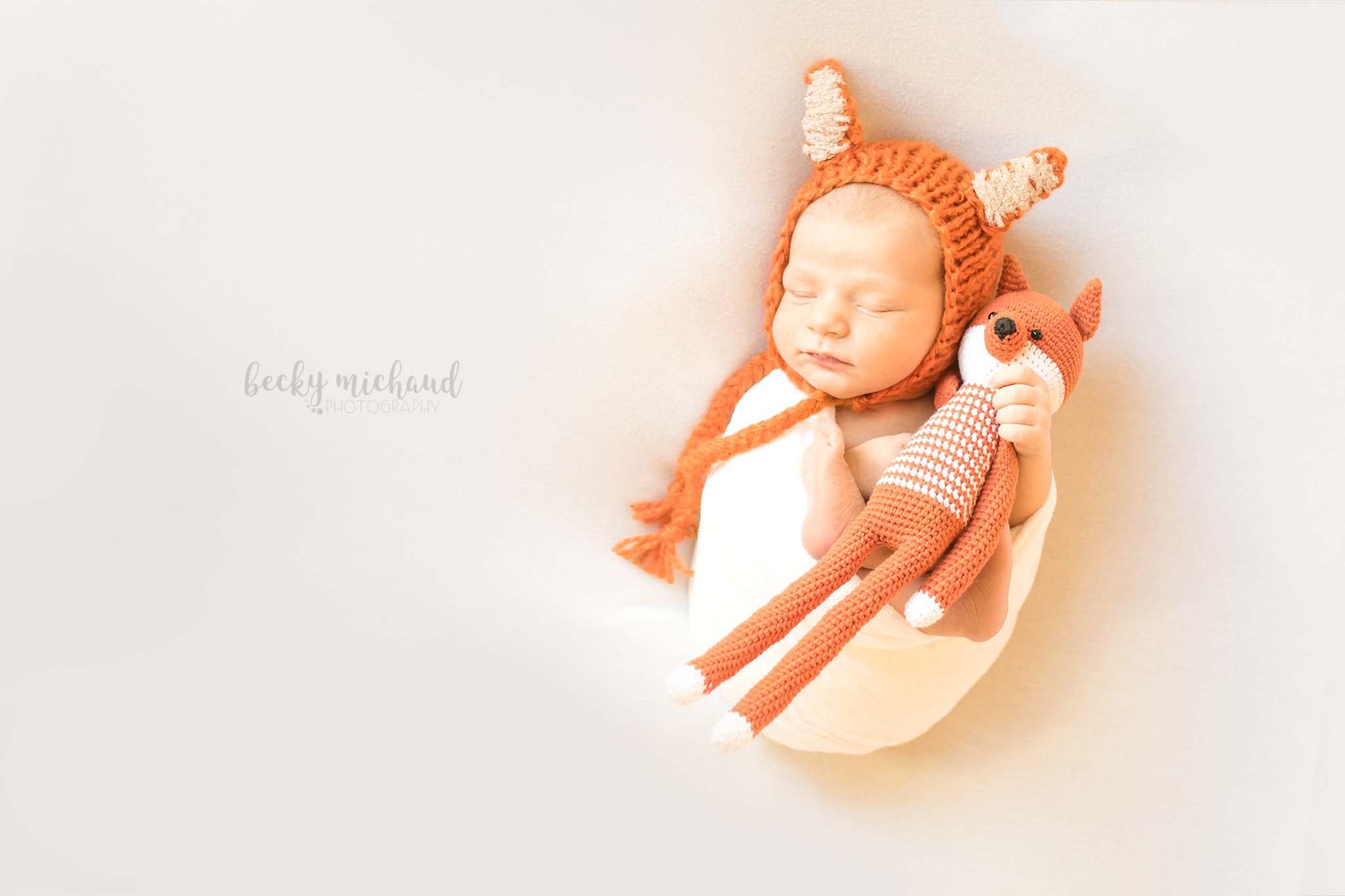 Newborn photo by Becky Michaud, Northern Colorado photographer, of a baby wearing a fox bonnet and holding a fox toy
