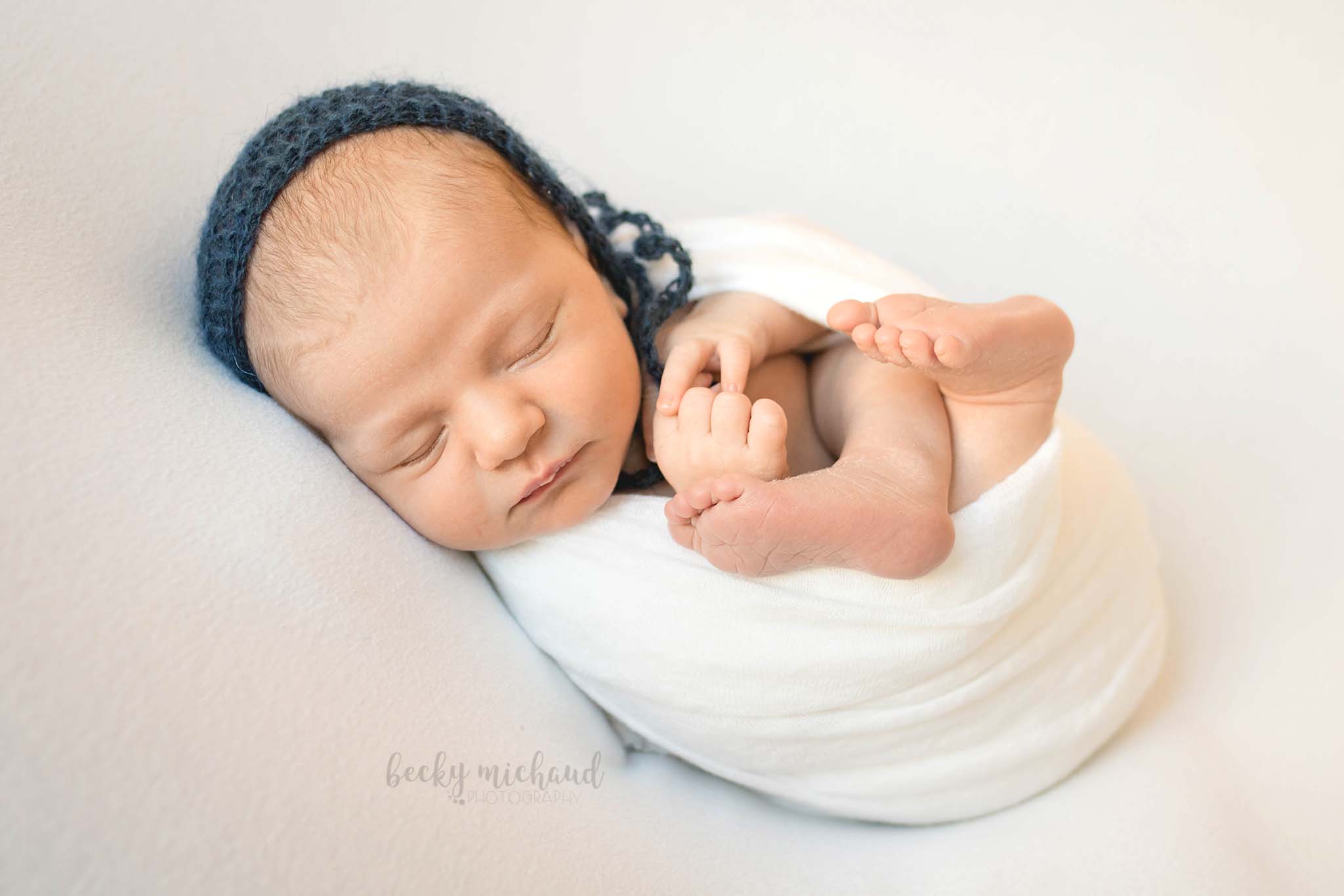 simple newborn photo of a baby on a white blanket wearing a blue bonnet in Fort Collins, Colorado