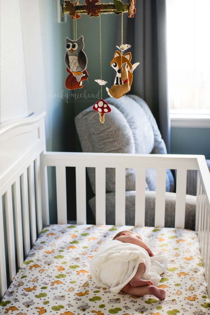lifestyle photo of a baby in his crib with a woodland themed mobile