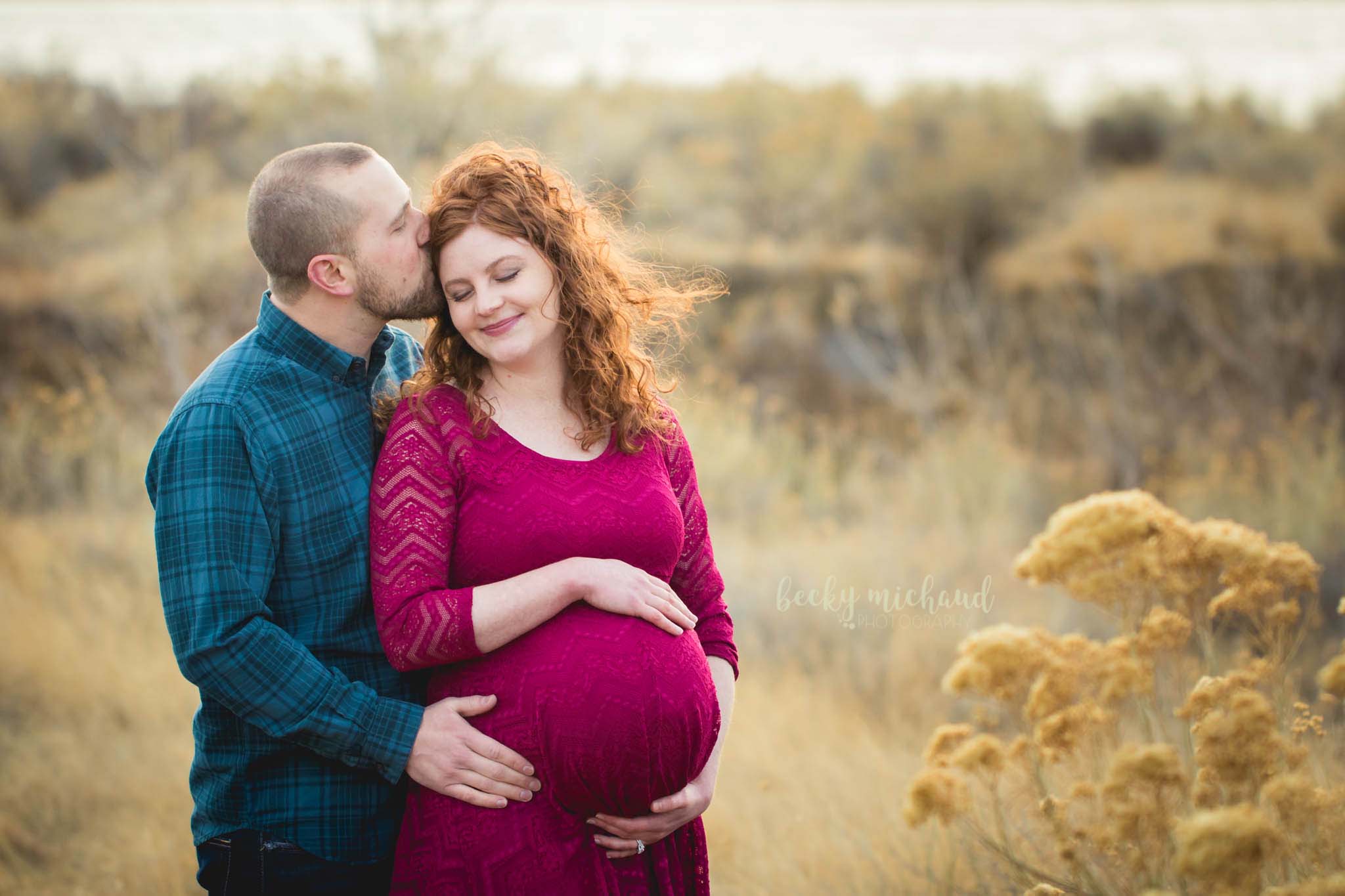 A husband kisses his wife's head during their maternity photo shoot