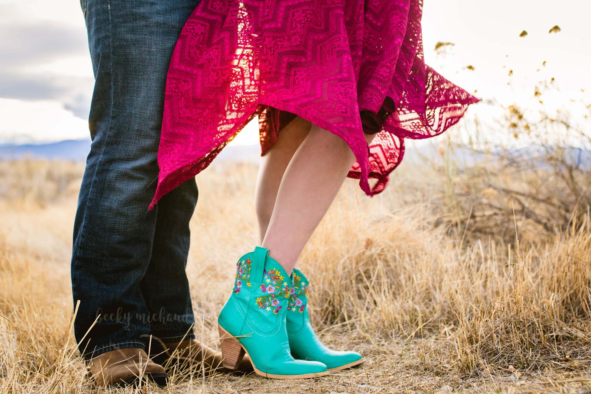 a couple's feet in cowboy boots with skirt blowing in the wind