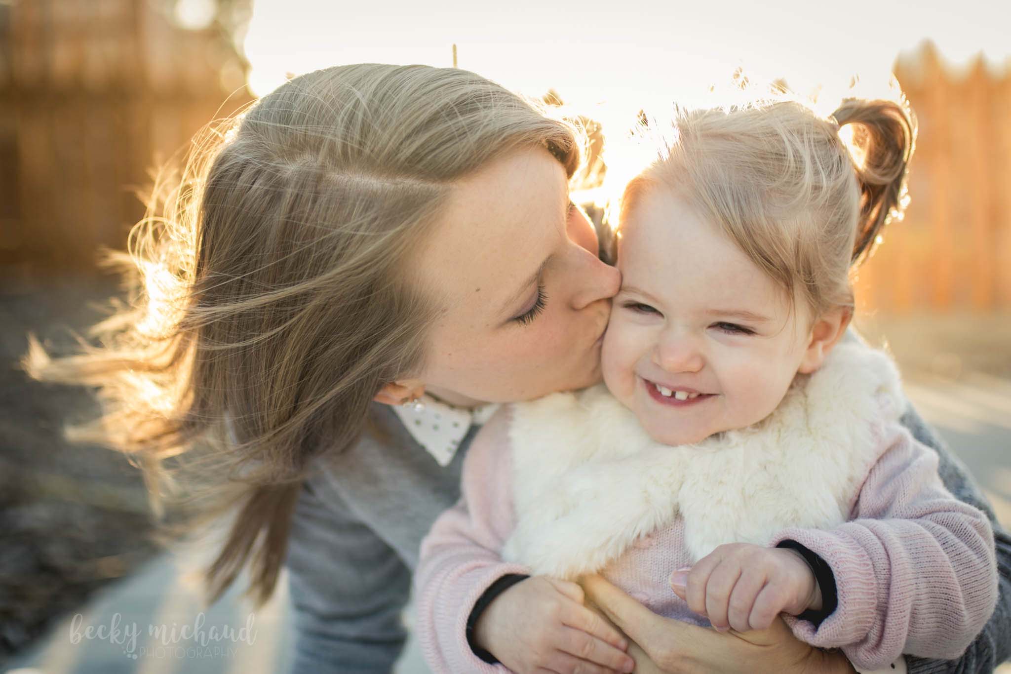 mama kissing her daughter's cheek in beautiful golden light during a photo session by Becky Michaud, Fort Collins photographer