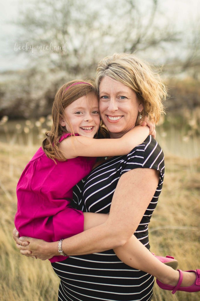 little girl sits on her mom's belly during their outdoor maternity photo session