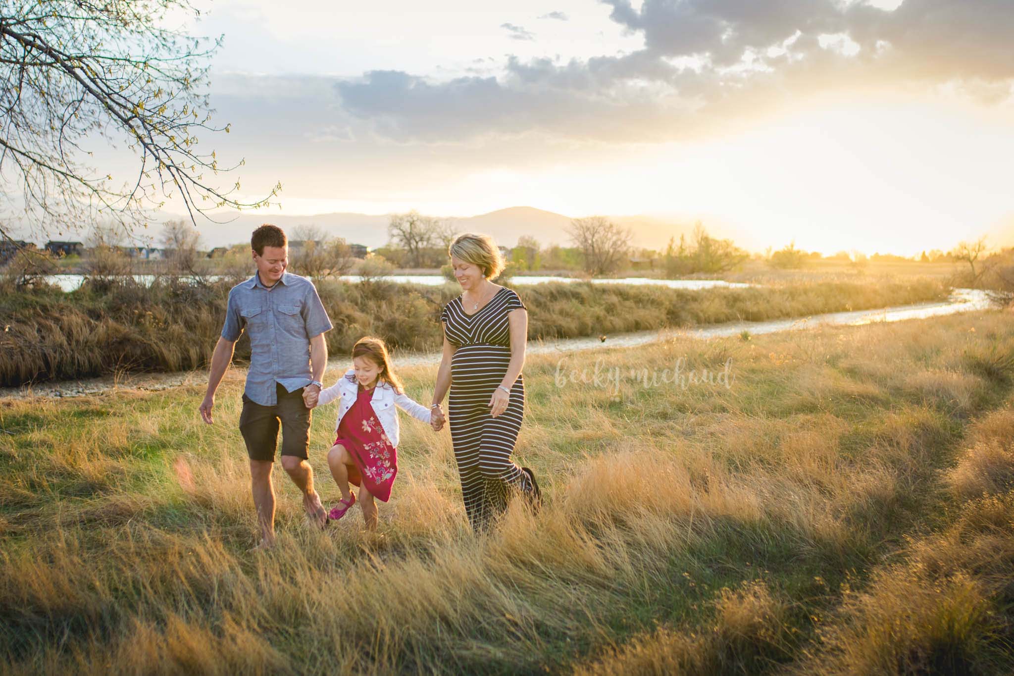 A couple walks through a field with their little girl and a baby on the way