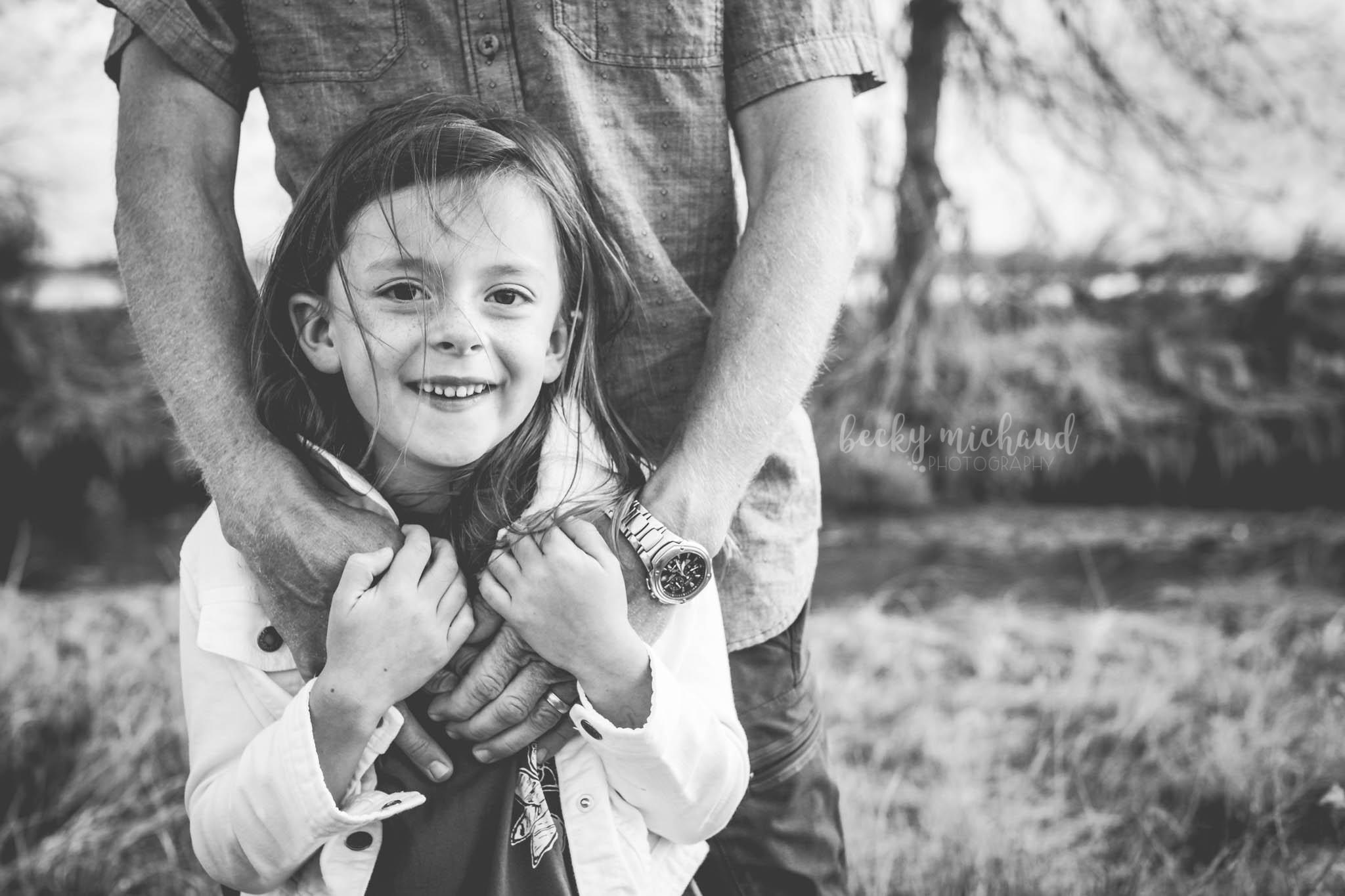 A young girl holds her dad's hands while he hugs her