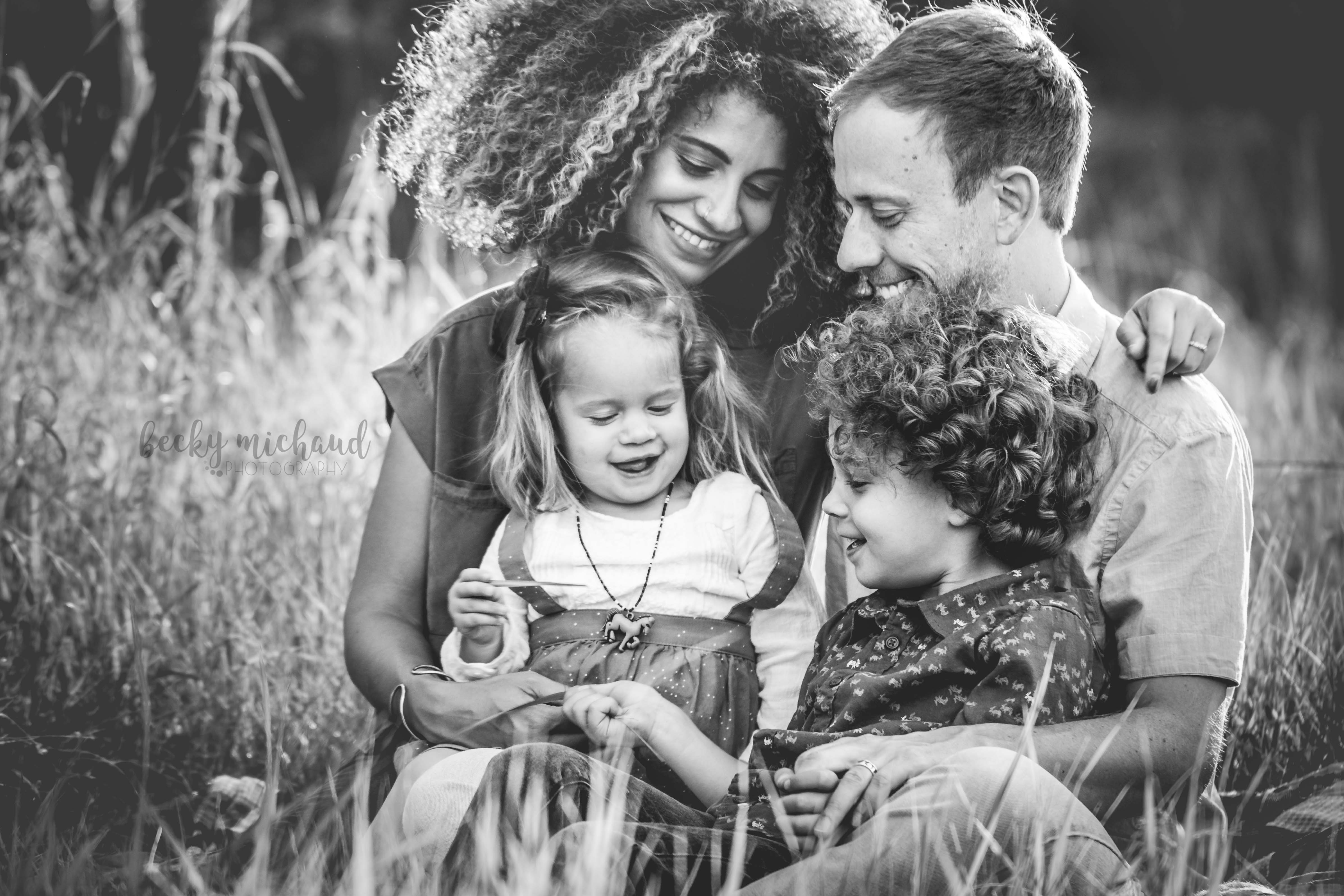 monochrome portrait of a family of four snuggled together in a field in Fort Collins