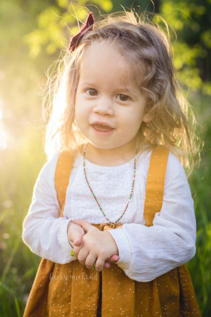 a toddler girl in a yellow dress poses for her portrait taken by Becky Michaud, a child photographer in Fort Collins, CO