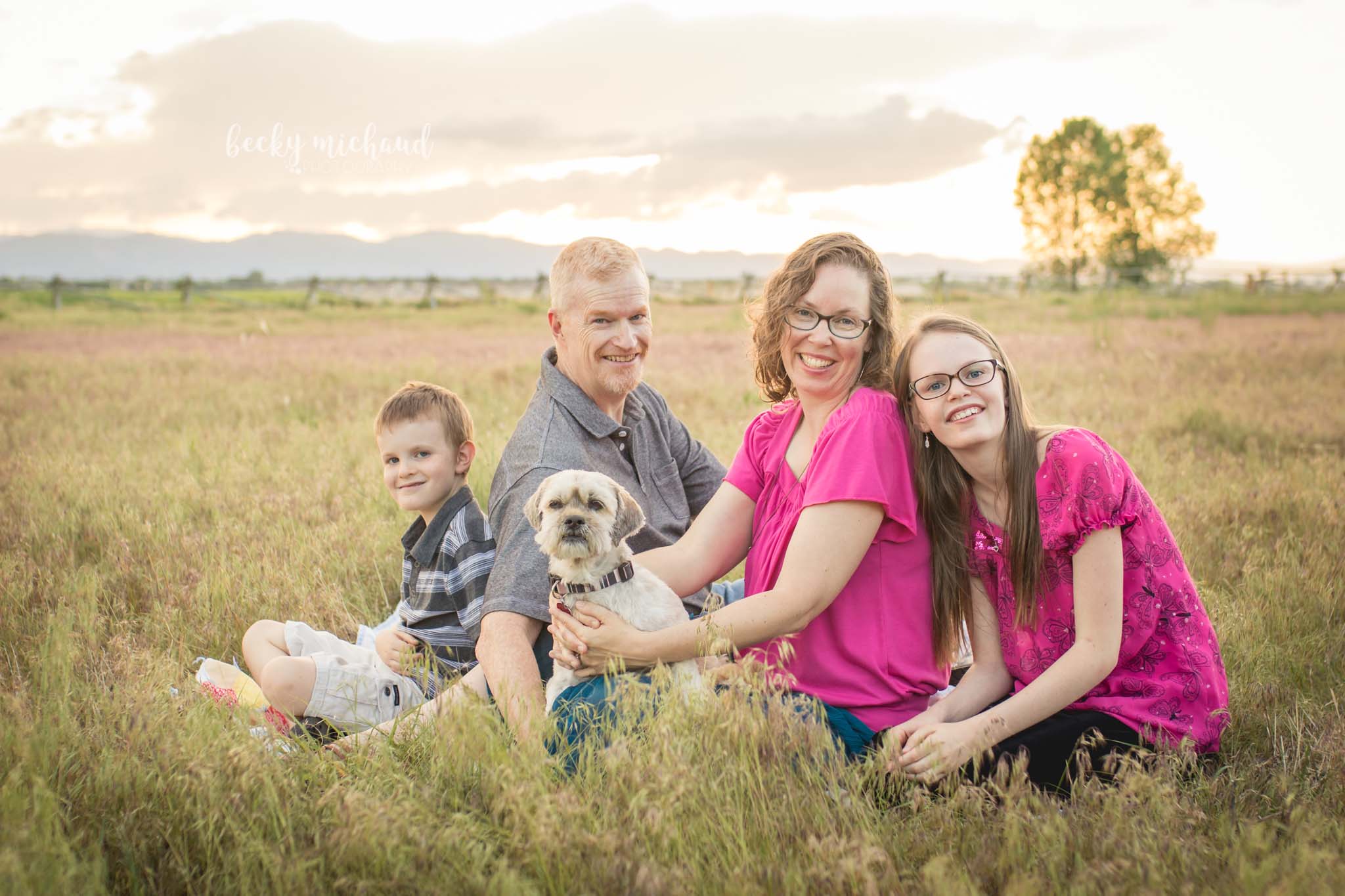 A family of four poses with their dog in a field in Fort Collins with the mountains in the background