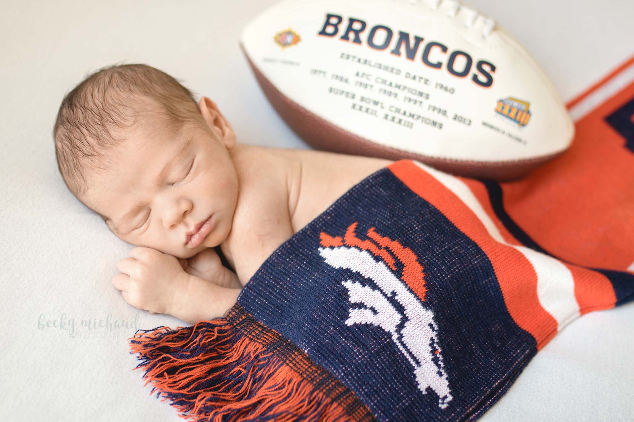 newborn baby posing with a Broncos football and team logo scarf