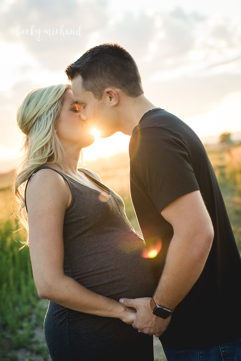 maternity photo of a couple kissing with sunflare