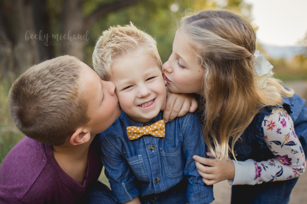 Big brother and sister kiss little brother on the cheeks during their family photos with Becky Michaud, Fort Collins photographer