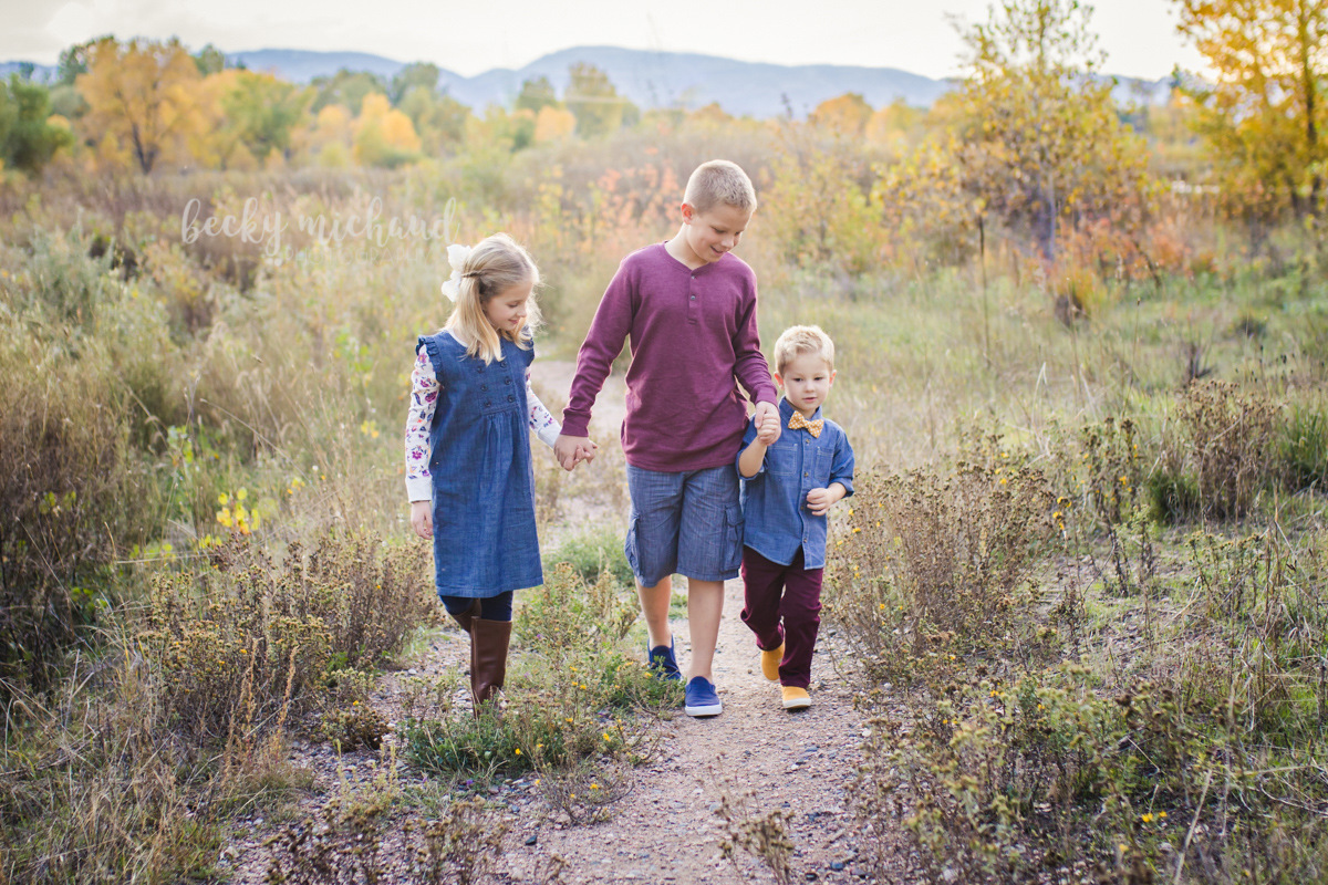 Three siblings walk together through a field in beautiful Colorado in the fall