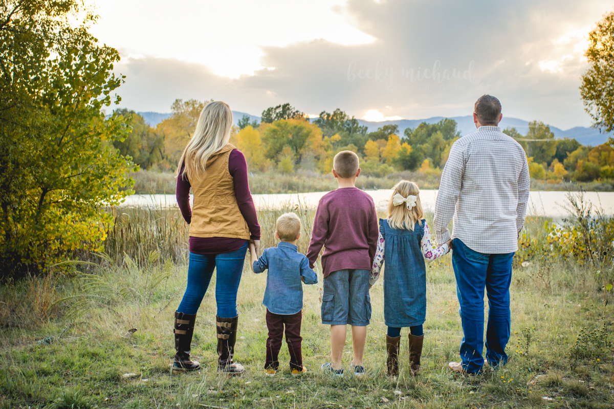 A family holds hands and gazes across a pond as the sunsets over the Colorado mountains