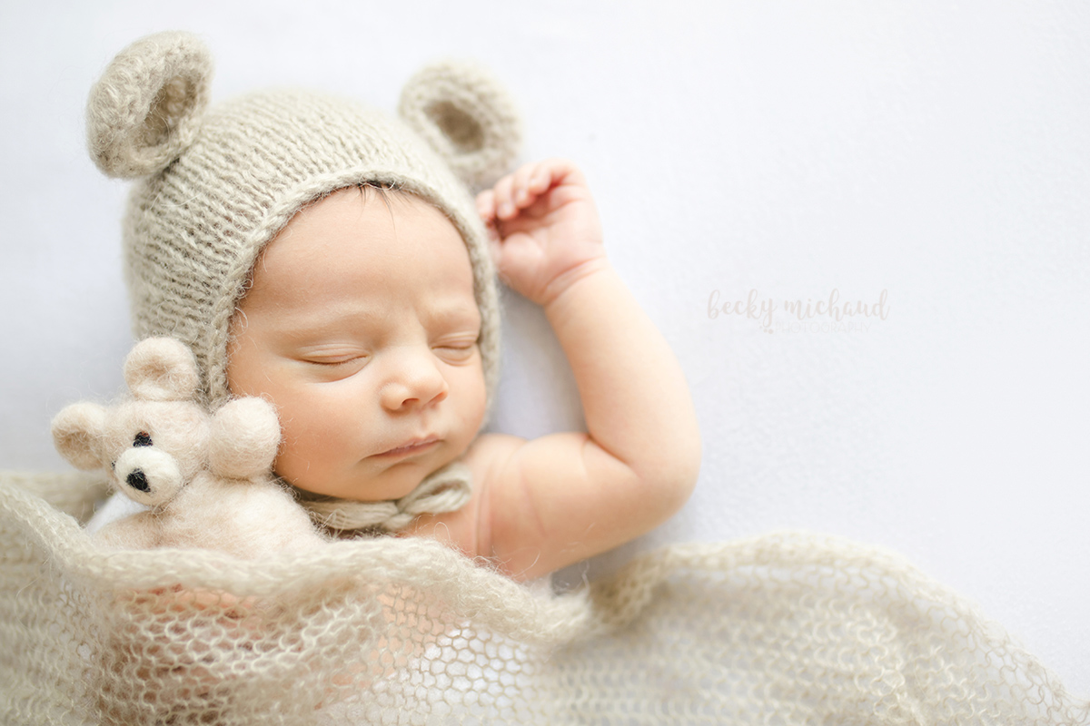 Newborn baby wearing a bear hat and holding a stuffed bear