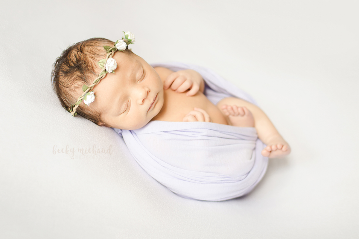 Baby girl posing for her newborn photo session with a lavender wrap and floral crown