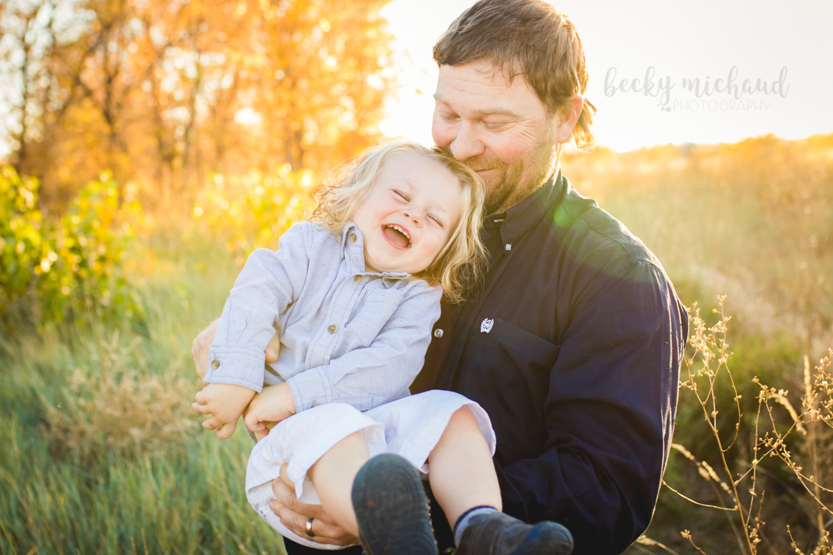 A dad plays with his toddler son during their family photo session at Arapahoe Bend in Fort Collins