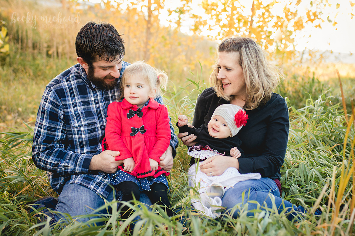 A family of four sits in the grass by the yellow aspen trees for their session with Fort Collins Photographer, Becky Michaud