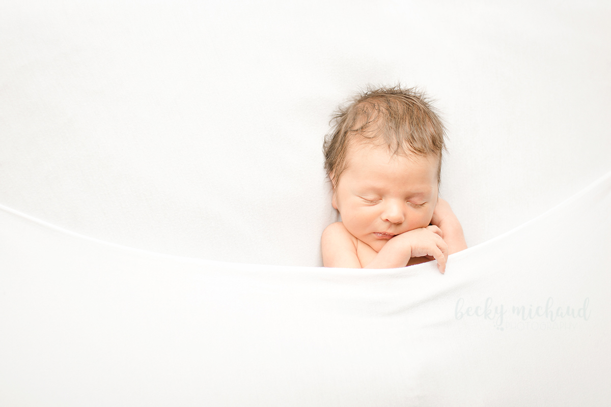 Minimalist newborn photo of a baby tucked under a white blanket