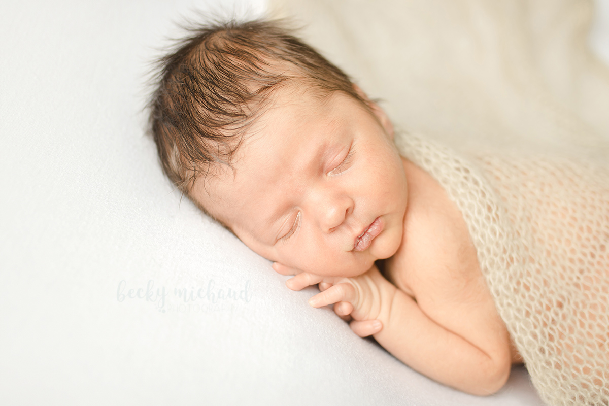 Newborn baby sleeps under a knit blanket during his in home newborn photo session