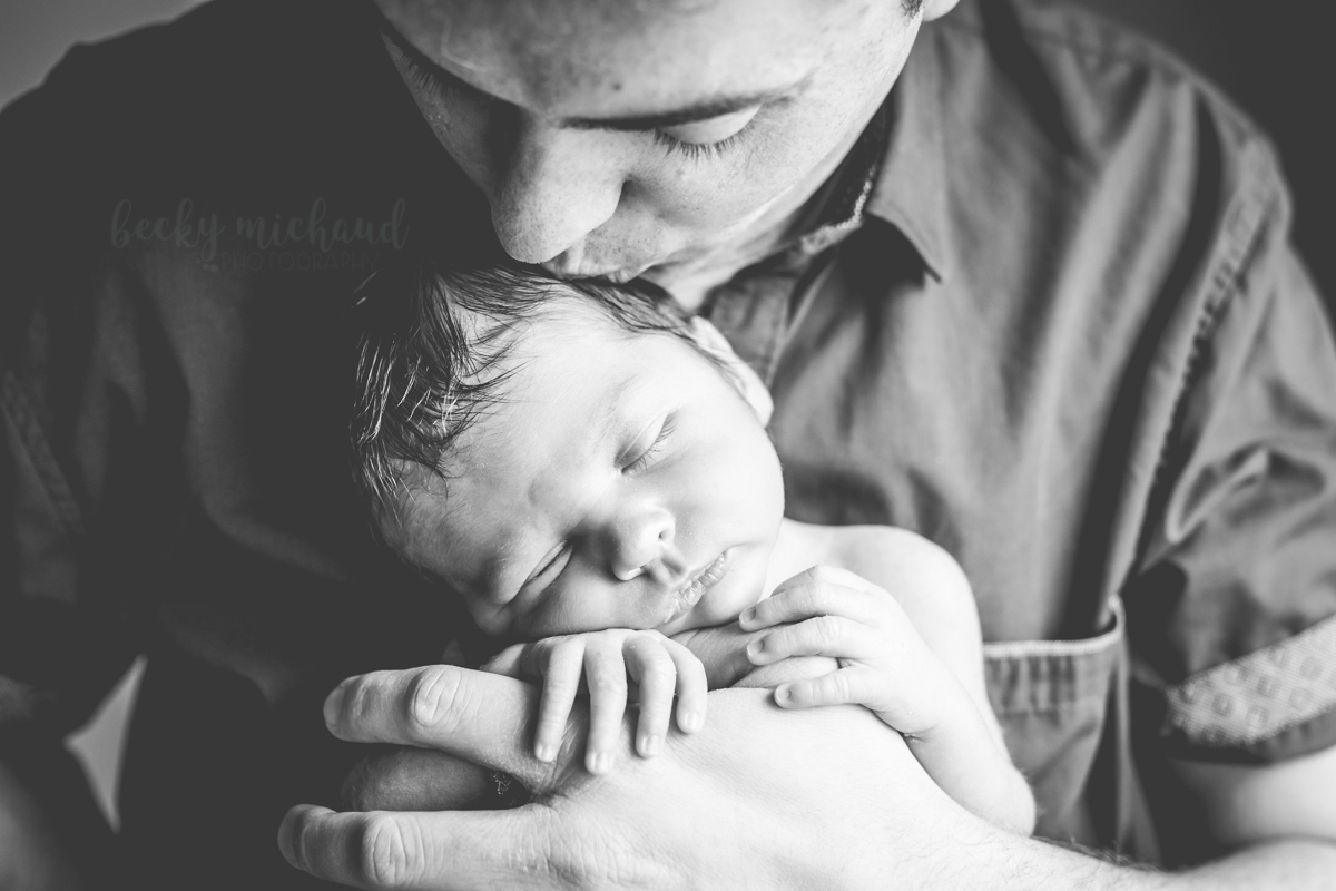 Black and white photo of a dad kissing his baby on his head