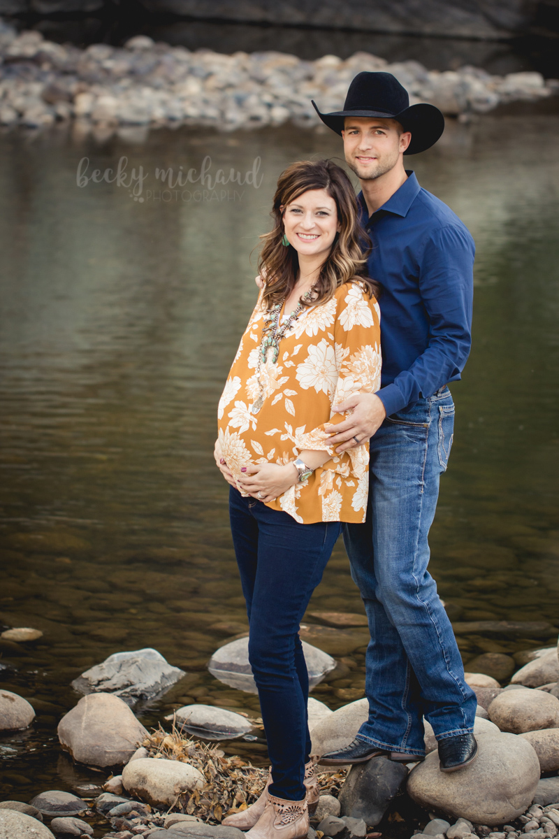 A couple poses for their maternity photo session by the Poudre River