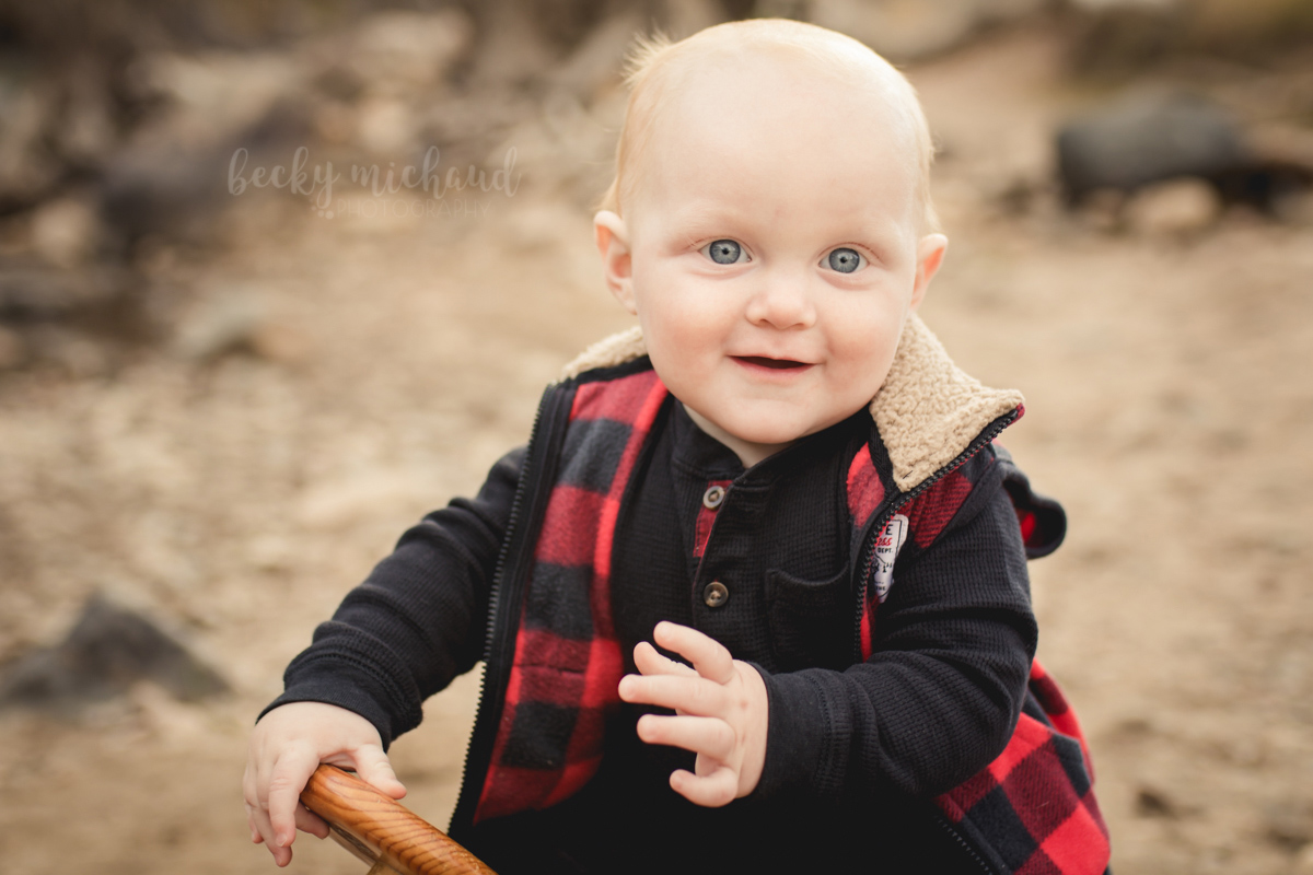Baby boy in a buffalo plaid vest smiles for his milestone photo session in the Colorado foothills