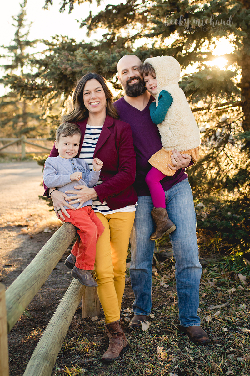 Family photo by a fence and evergreen tree at the Poudre ELC in Fort Collins, Colorado
