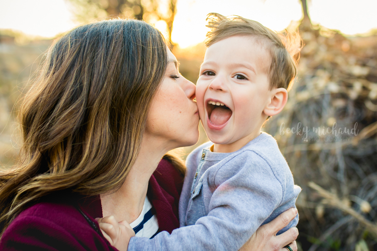 A boy looks surprised when his mom kisses his cheek 