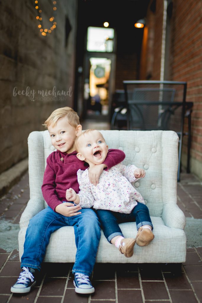 Two young siblings hug on a mini couch in an alley in Old Town Fort Collins
