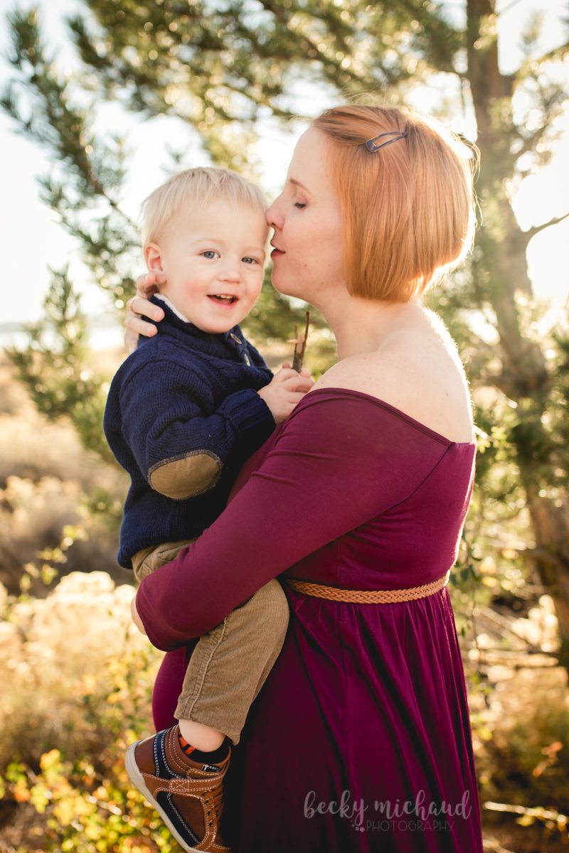 A mom kisses her toddler on the head during her Loveland Colorado maternity photo session