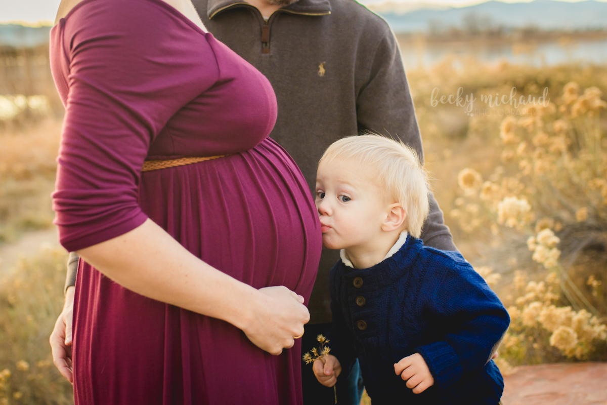 A toddler kisses his mom's belly while they poses for their maternity photos with Becky Michaud, Fort Collins photographer