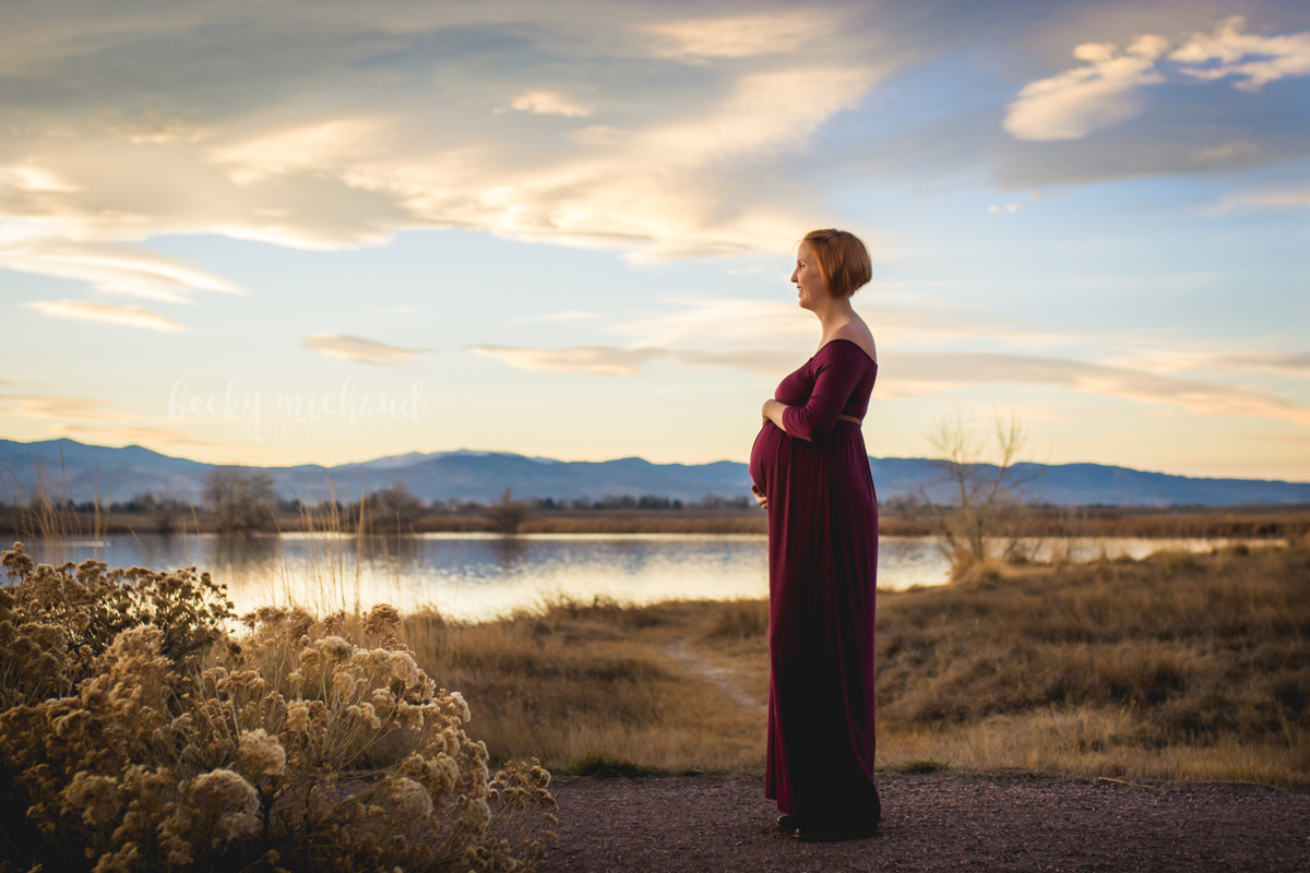 A beautiful pregnant mama stands by Equalizer Lake in Loveland Colorado while the sun sets in the background