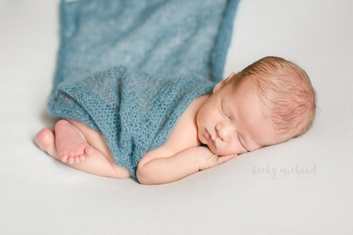 Simple newborn portrait of a baby on a white backdrop with a blue blanket