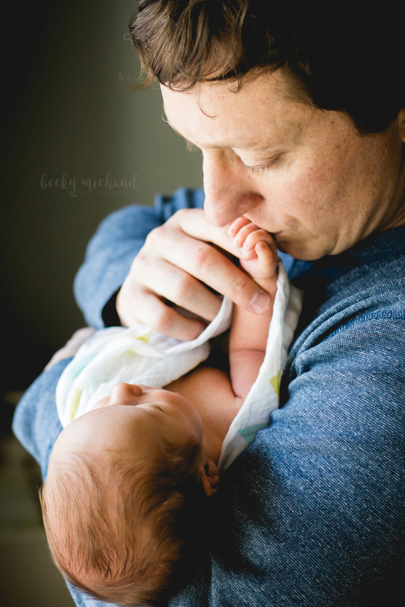 Dad kisses his new son's hand during their Windsor Colorado newborn lifestyle photo shoot