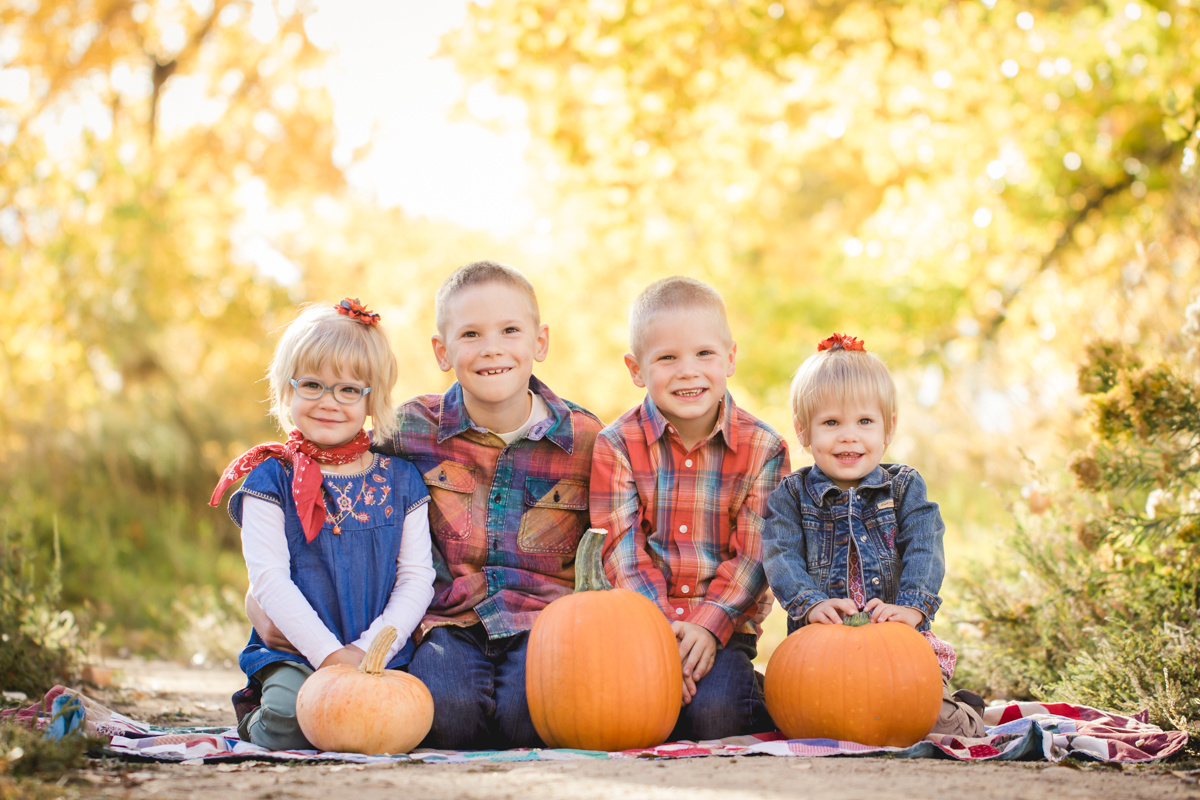 Four siblings pose with pumpkins during their fall family photo shoot at Arapahoe Bend in Fort Collins
