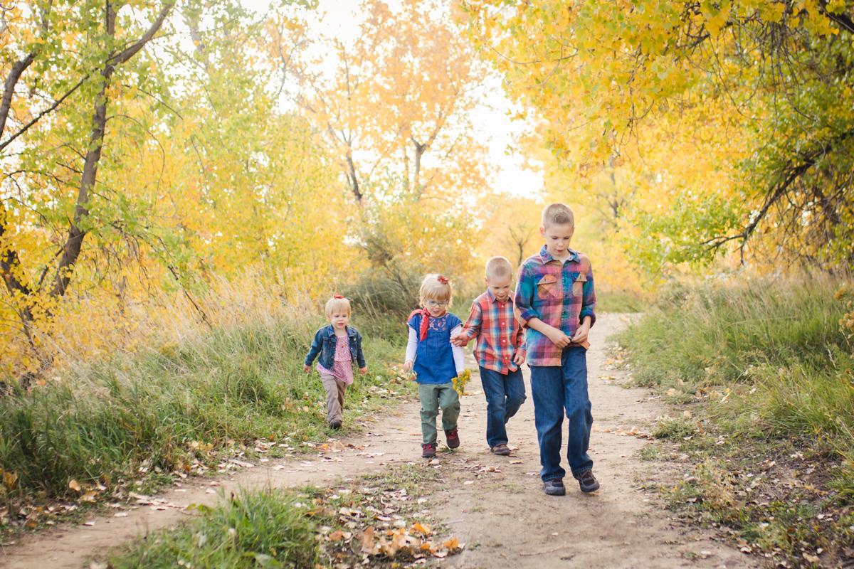 Four siblings play follow the leader on a wooded path in the fall