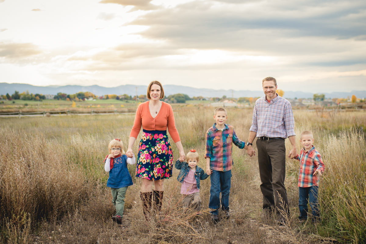 A family of six walks in a field with the Colorado foothills in the background