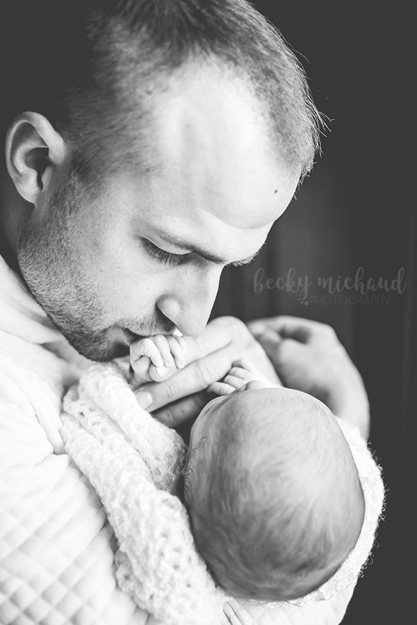 A father kisses his baby's hand during their newborn photo session in Fort Collins