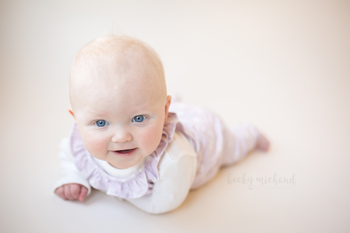 A six month old girl smiles on a white backdrop