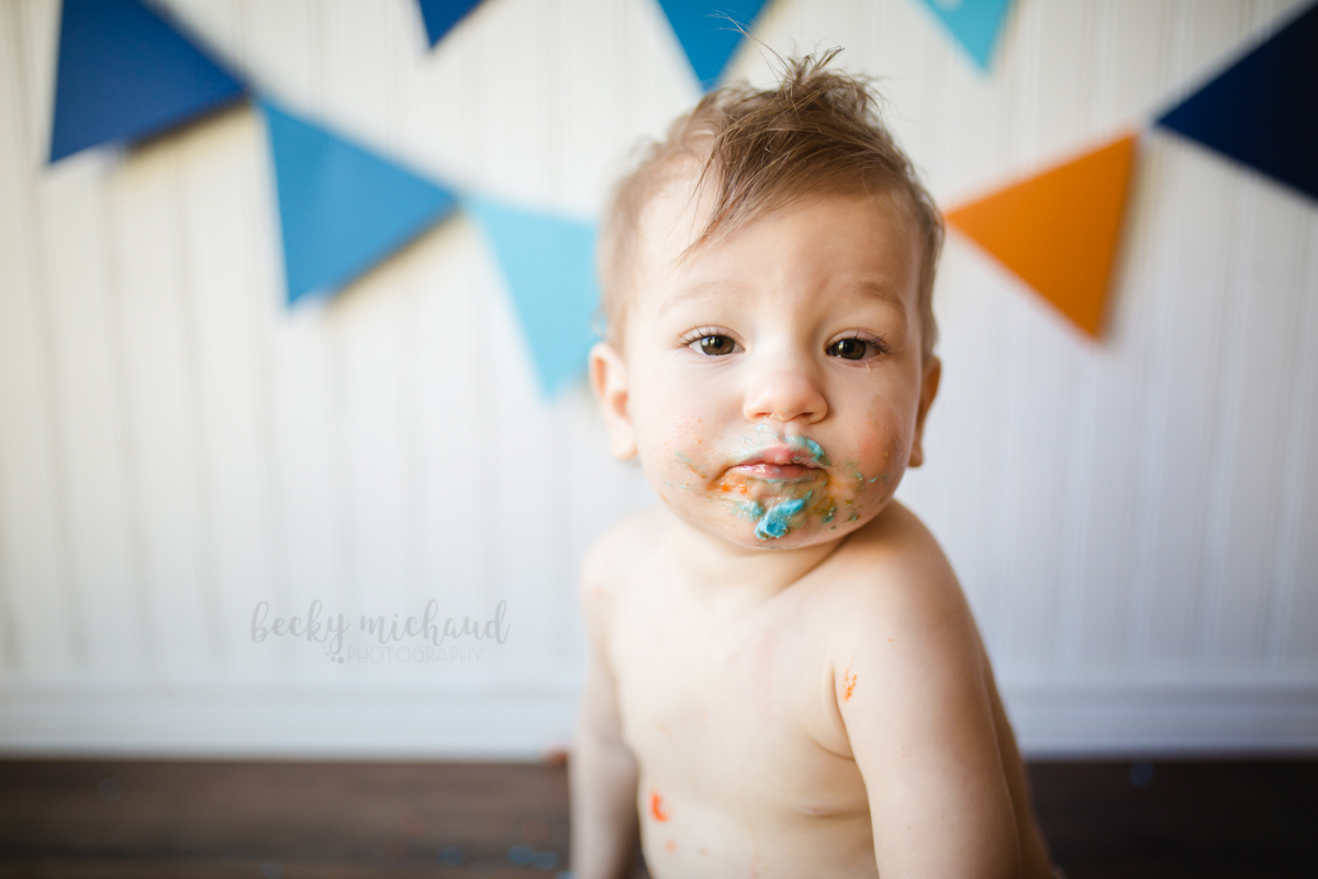 A frosting covered little boy pauses to look at the camera during his cake smash photo shoot in his Fort Collins home