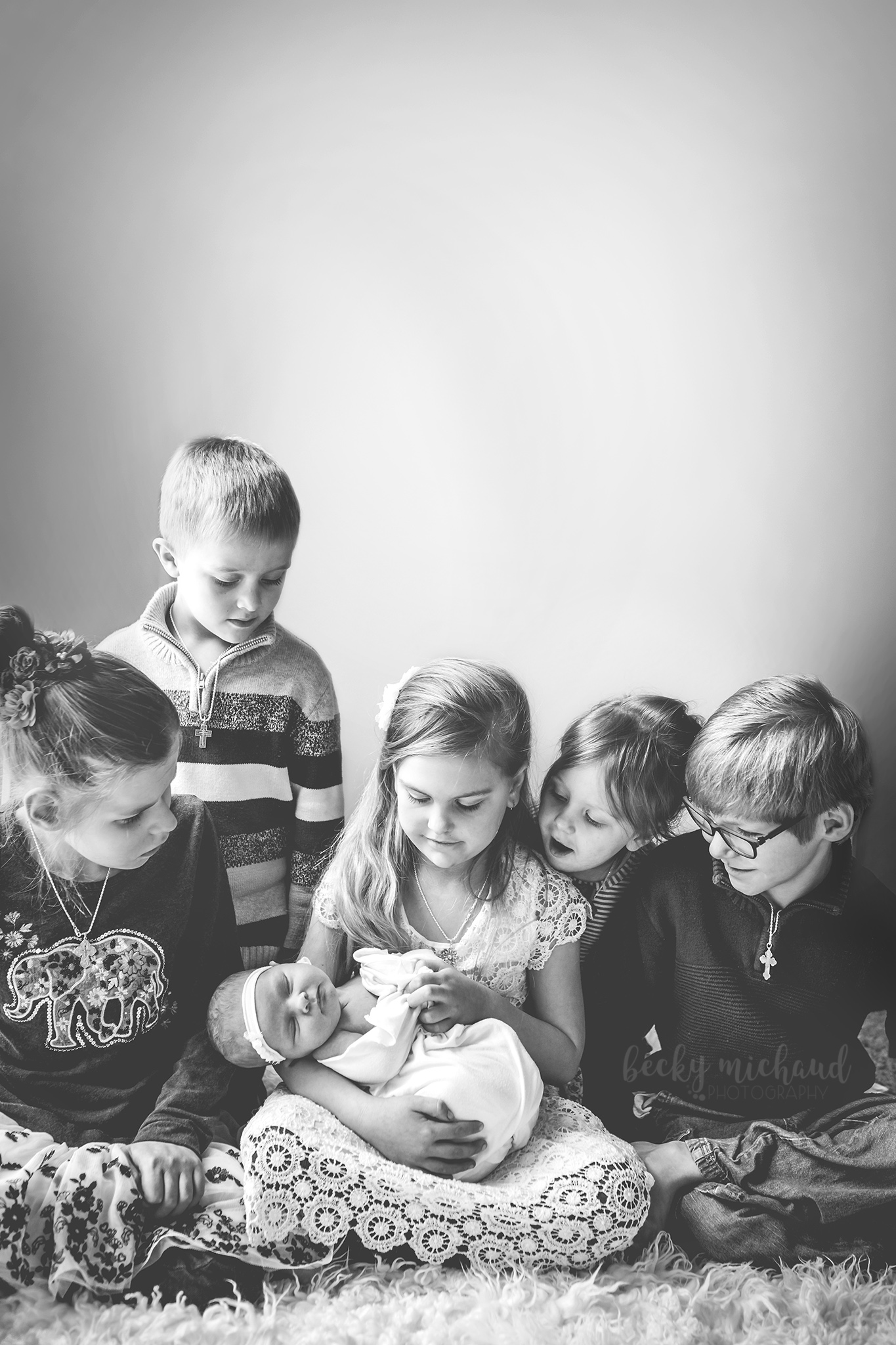 Black and white photo of siblings crowded around their newborn baby sister in their Loveland, Colorado home