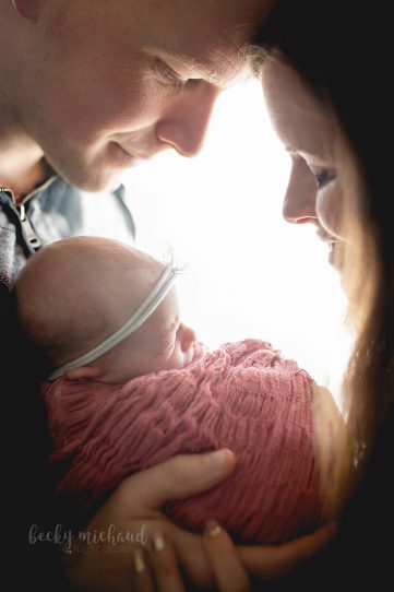 backlit photo of a mom and dad holding their newborn baby girl in their Windsor, Colorado home