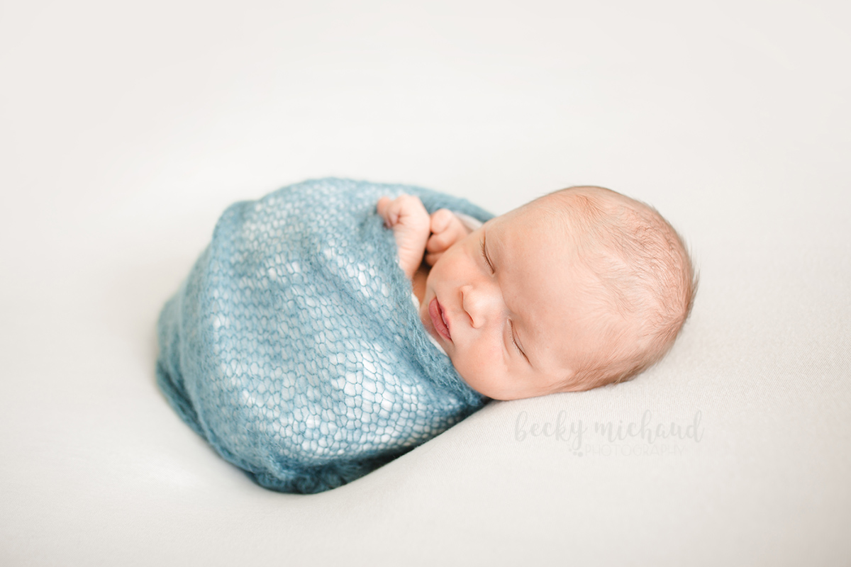 Photo of a newborn boy wrapped in a blue blanket taken by Becky Michaud, Northern Colorado baby photographer
