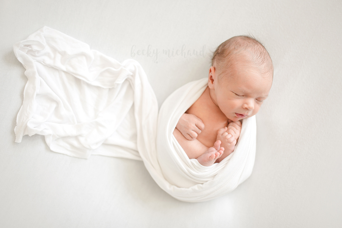 baby wrapped in white blanket on a white backdrop during his Fort Collins newborn photo session
