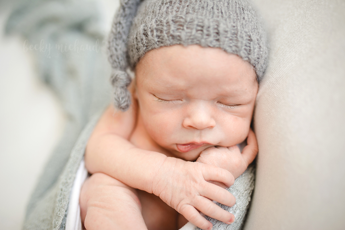 A baby boy wearing a grey slouch hat poses for newborn portraits