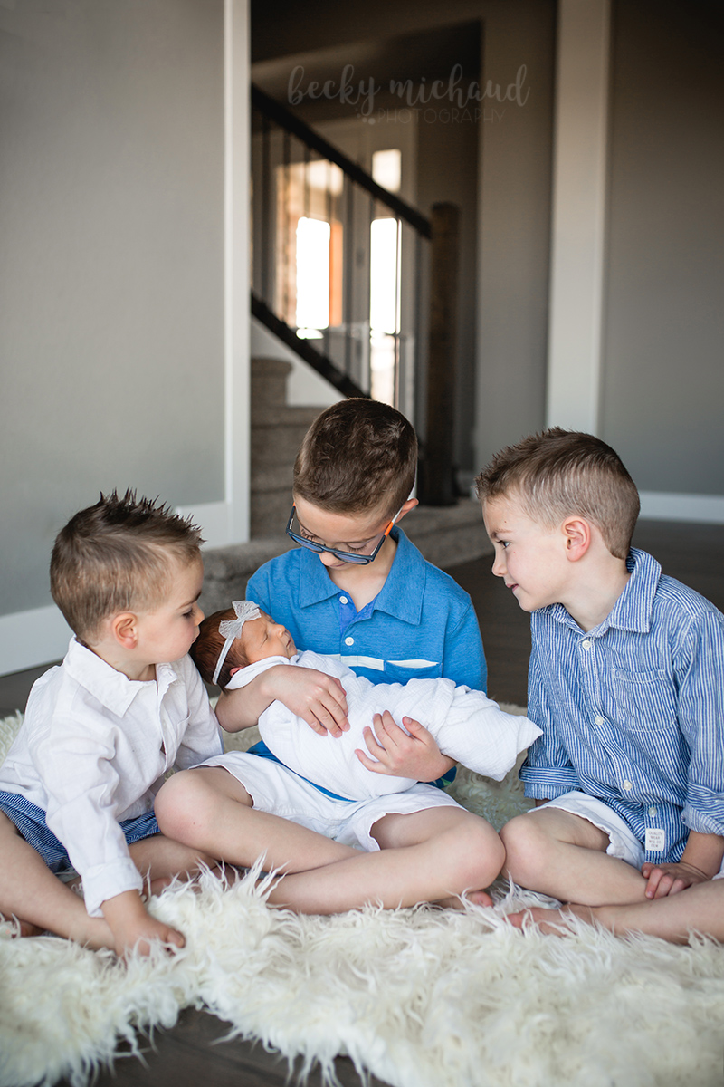 Three brothers hold their new baby sister during their in home newborn photography session in Loveland, Colorado