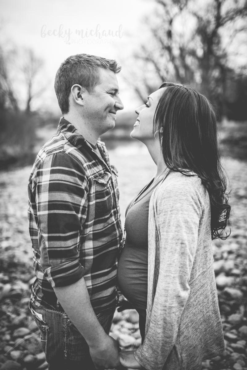 Black and white photo of a couple smiling at each other in anticipation of their new baby