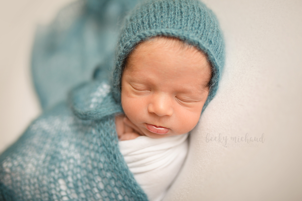 A baby wearing a blue knit bonnet and wrap pouts during his newborn photo session in Fort Collins